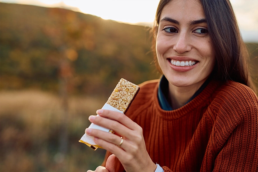 Smiling young woman eating a healthy snack bar